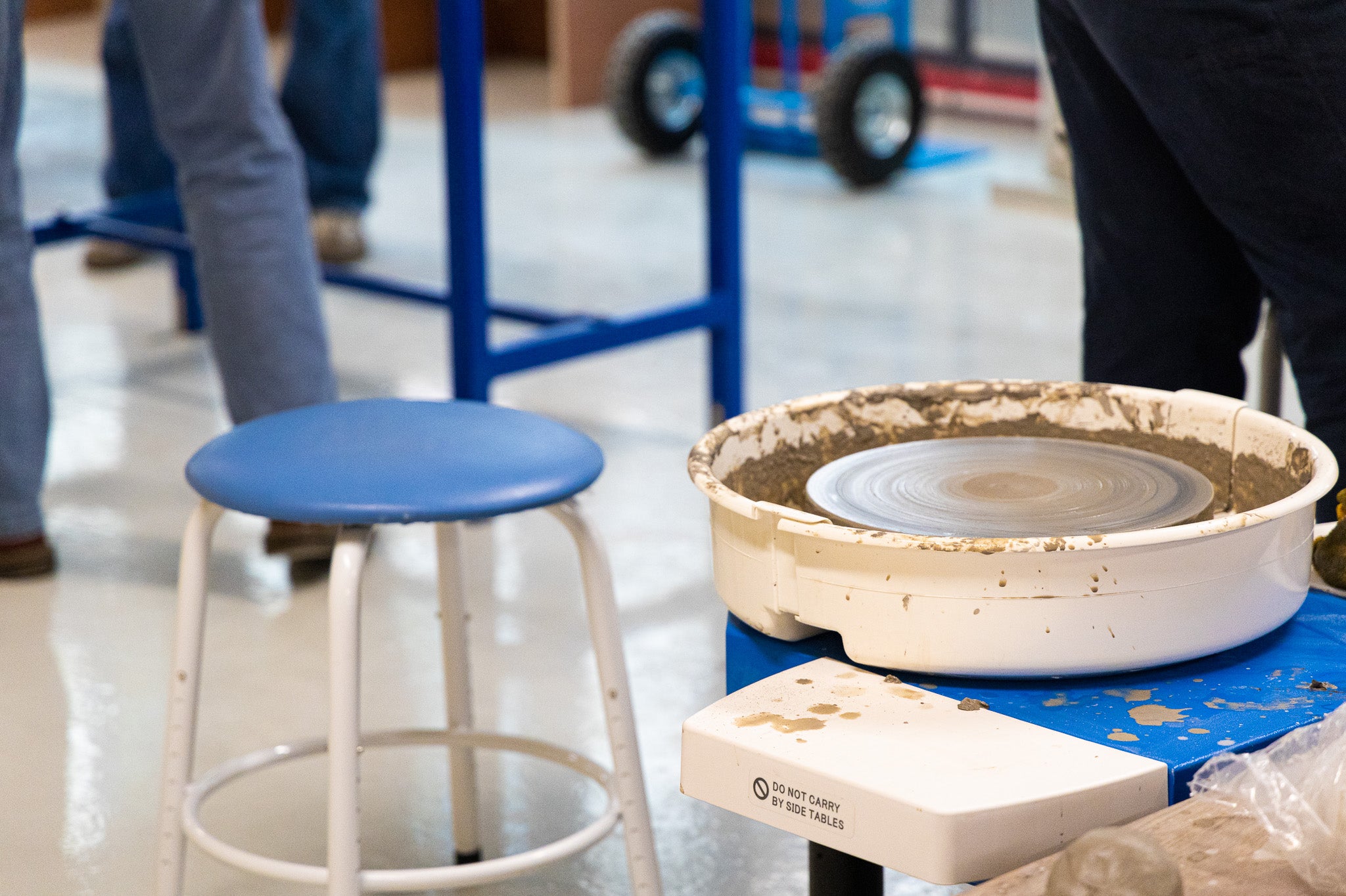 A pottery wheel stands beside a blue and white stool. Clay is seen on the wheel where it had just been used for throwing