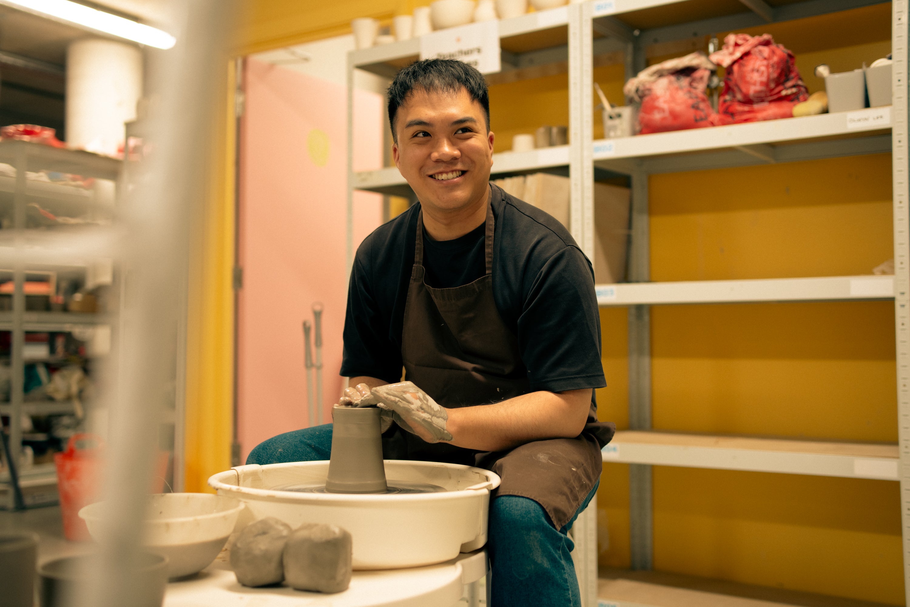 Throwing Shapes teacher Vinh smiles as he sits at the potter's wheel throwing a clay vase