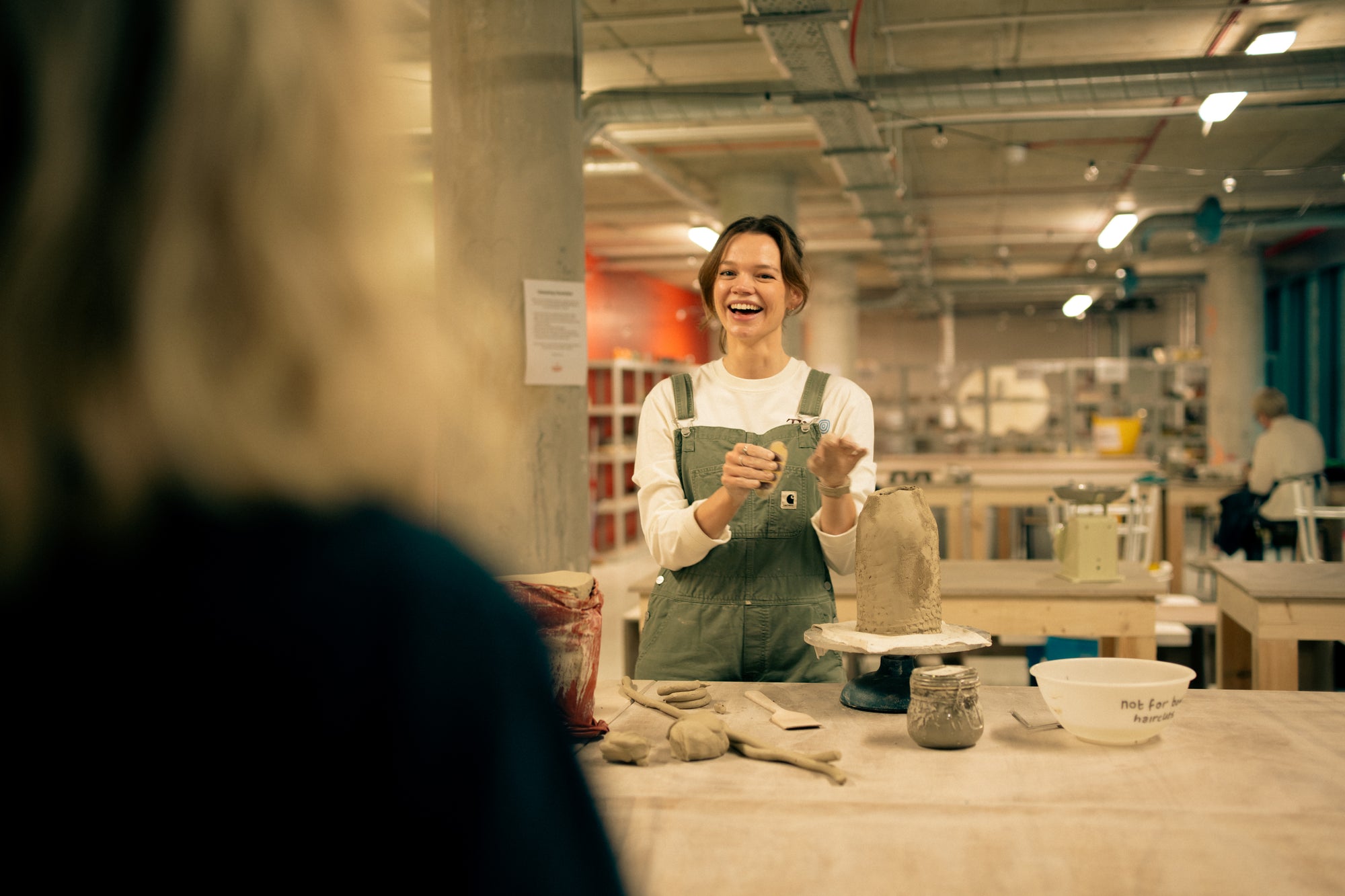 Throwing Shapes teacher Aine smiles at workbench whilst hand-building with clay. 