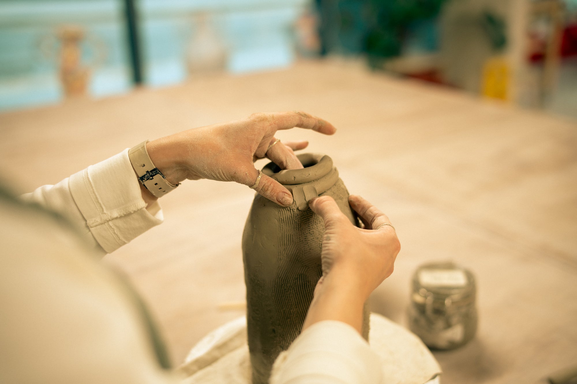 Throwing Shapes teacher Aine works at wooden bench hand-building a ceramic vase with dimpled textures.