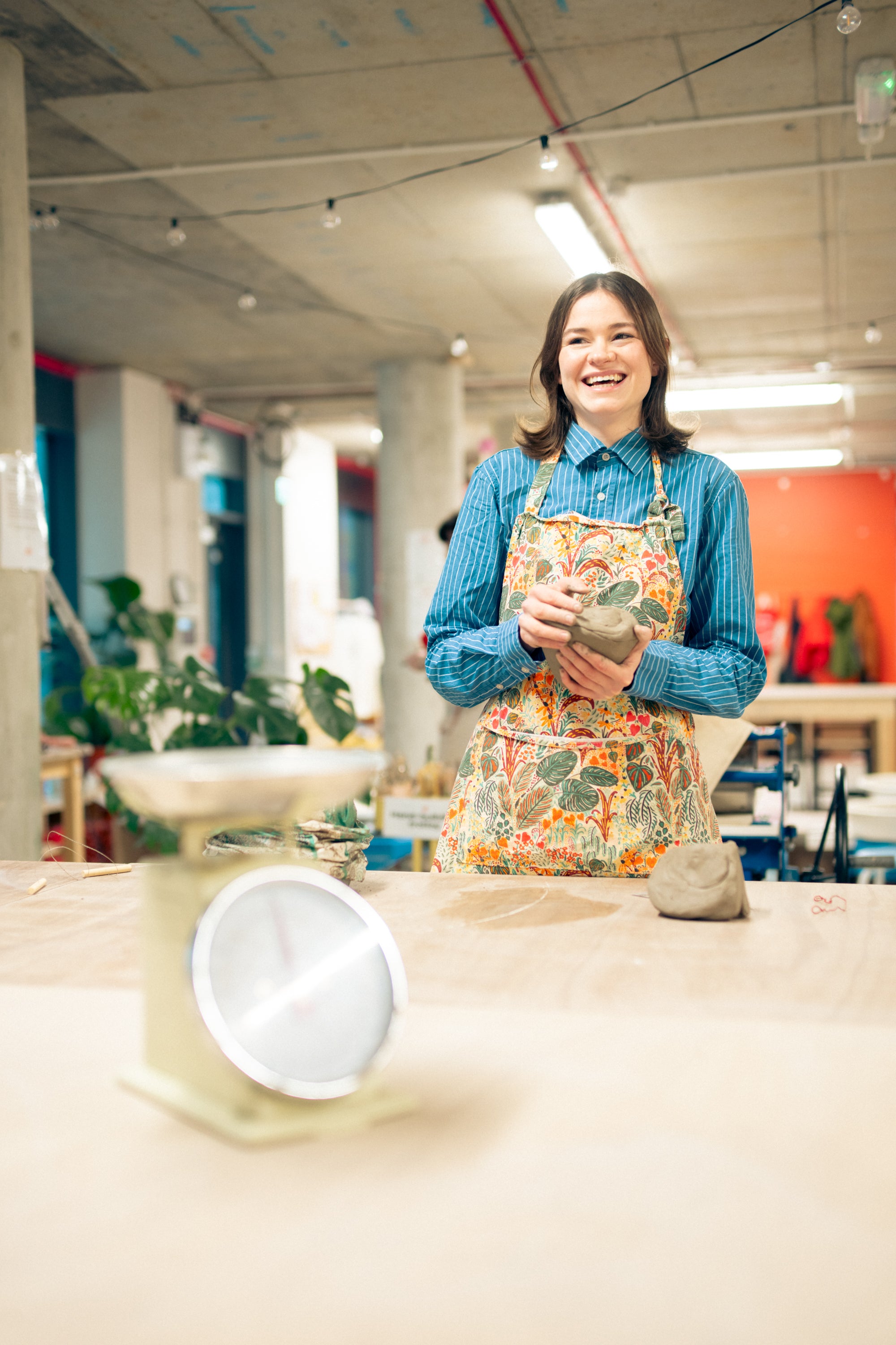 Throwing Shapes teacher Lily smiles holding clay ready for throwing. Scales are shown.