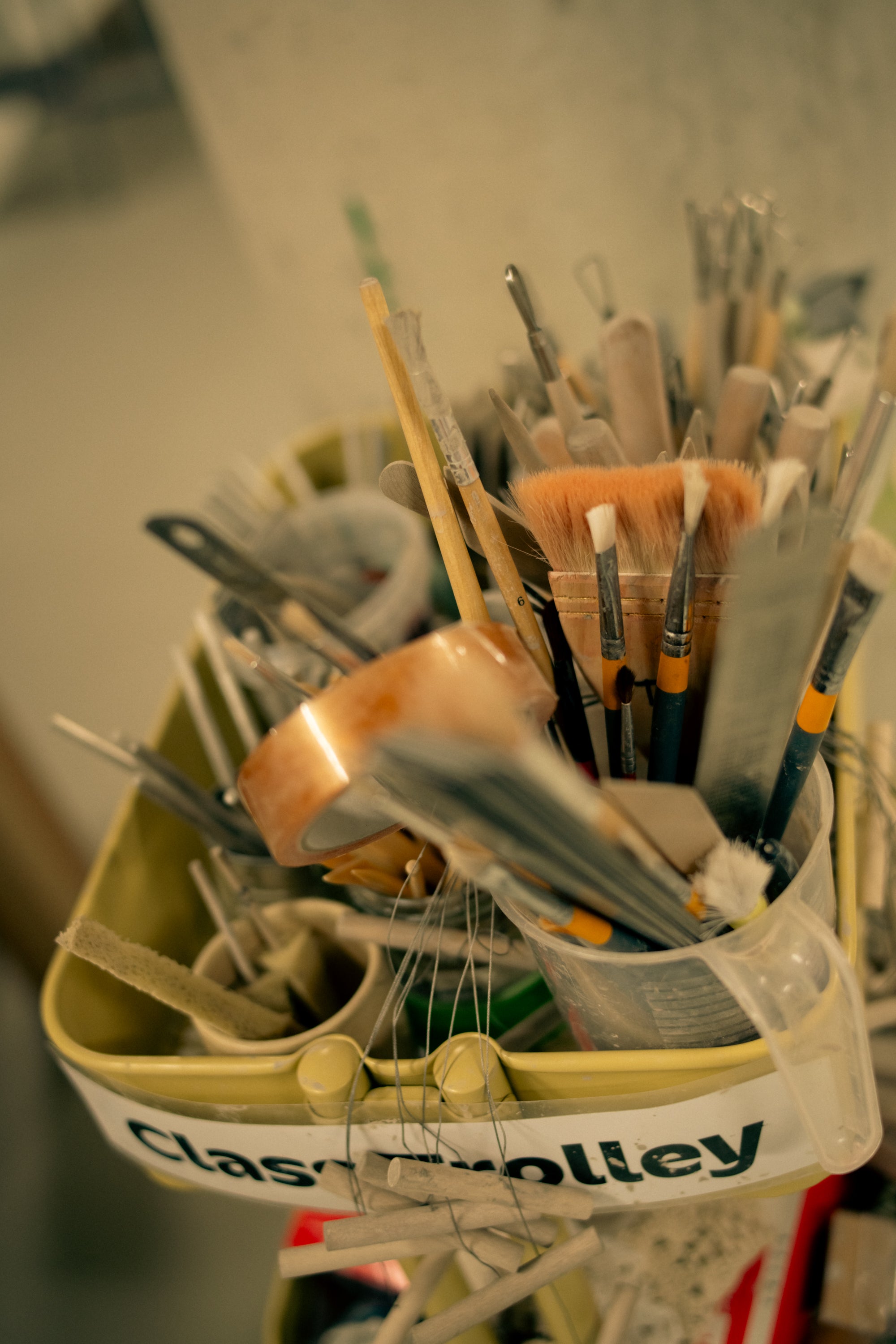 A collection of paintbrushes, tape, ribbon tools sits in a small yellow trolley with a sign that reads "class trolley" attached