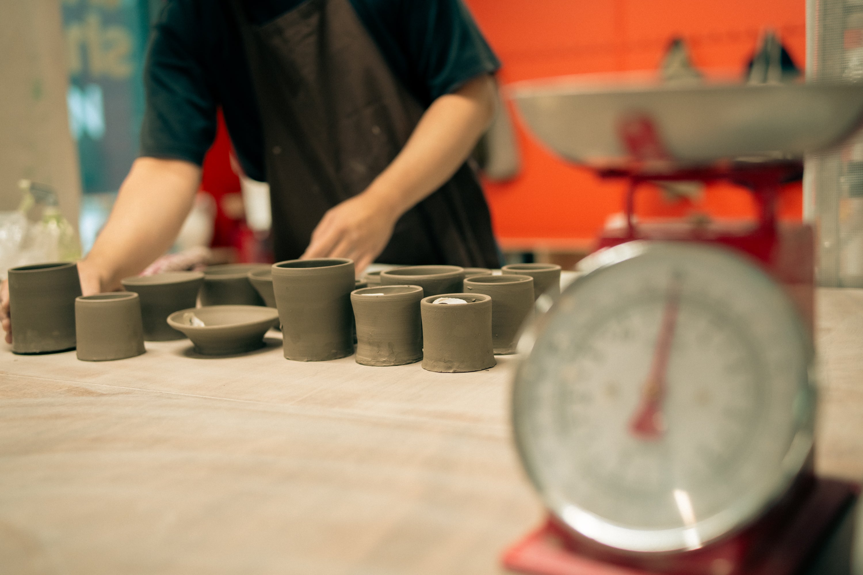 Multiple clay objects are lined up in front of a Throwing Shapes teacher. Traditional weighing scales are prominent in the image but out of focus 