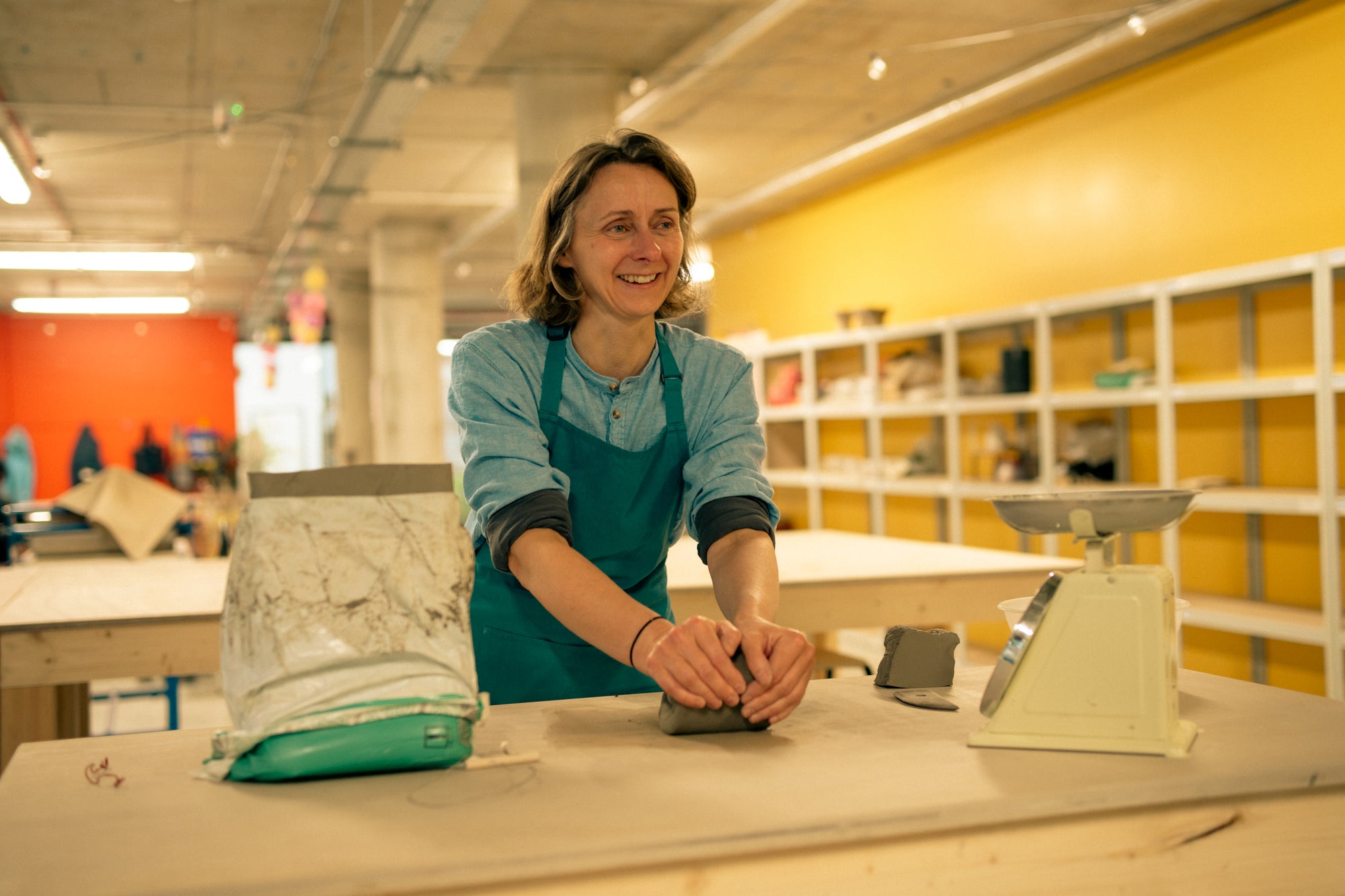 Throwing Shapes teacher Lucy works with clay on a wooden bench in a colourful pottery studio