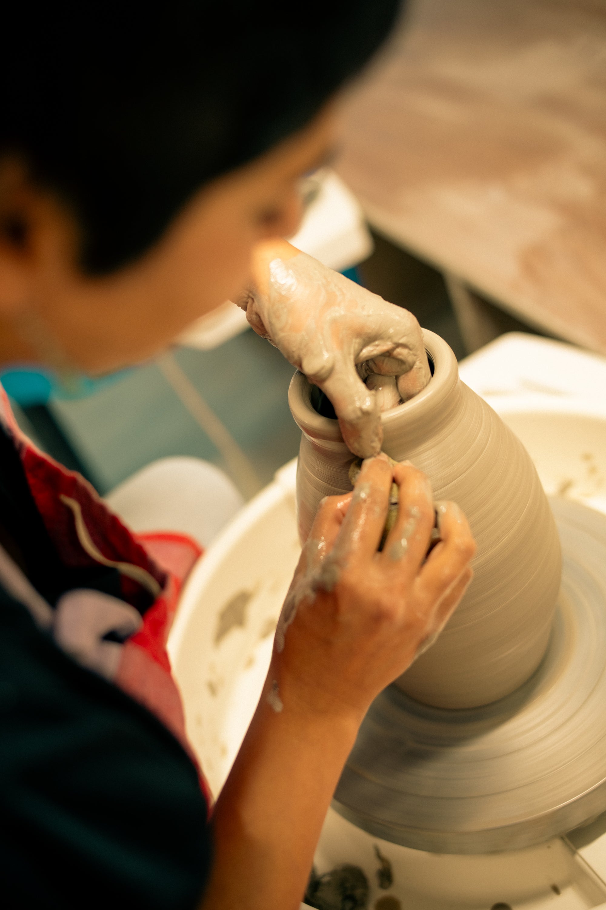 Throwing Shapes teacher Mahima pinches  the rim of freshly made clay vase on the potter's wheel