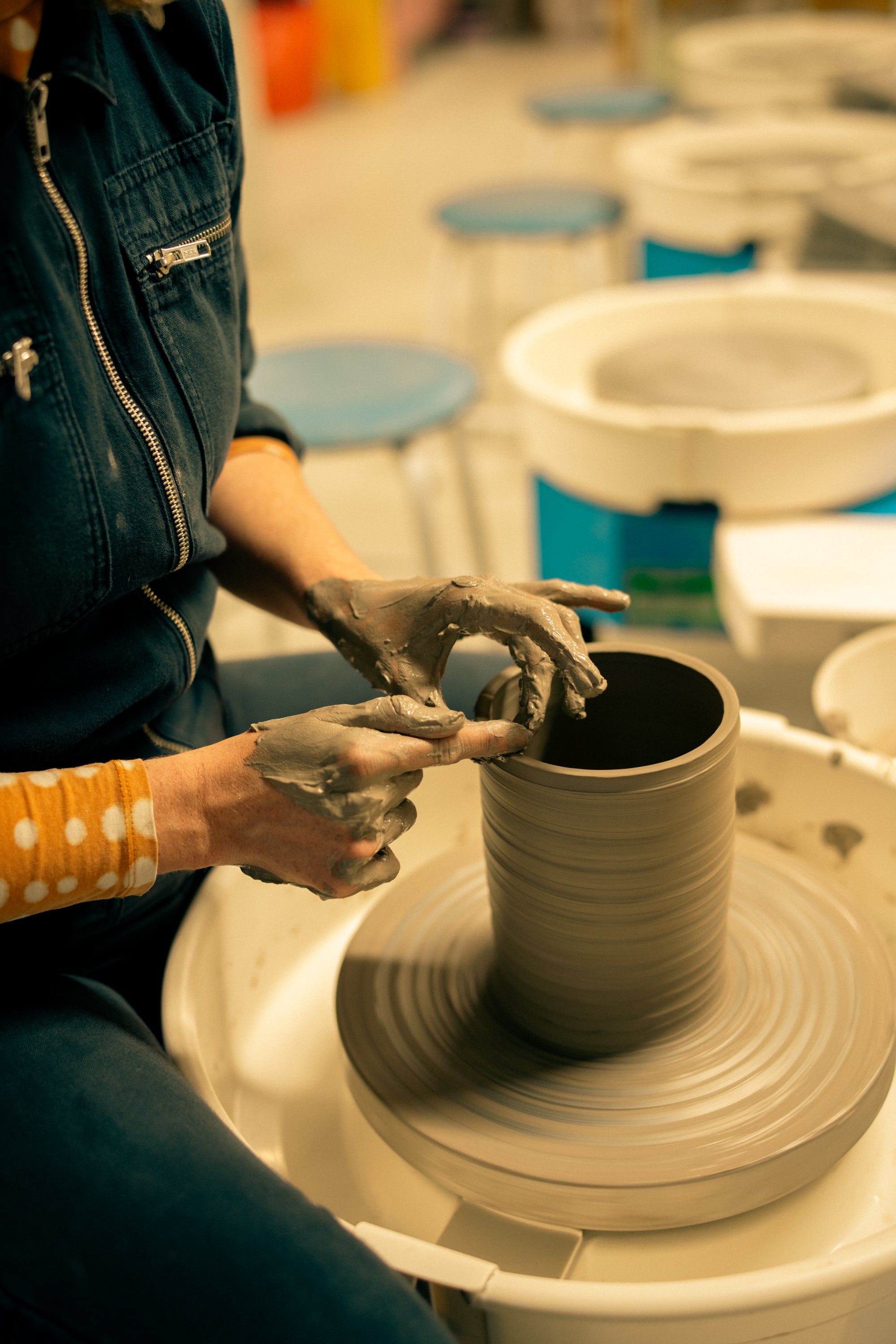 Throwing Shapes founder Siofra sits astride the potters wheel whilst turning a ceramic jar. 